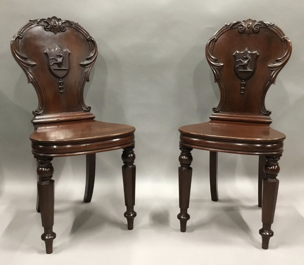 A pair of dark George IV mahogany hall chairs featuring carved backrest scrolls, crests depicting a hippocampus, and turned front legs. View II