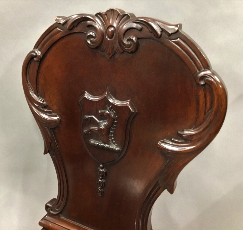 A pair of dark George IV mahogany hall chairs featuring carved backrest scrolls, crests depicting a hippocampus, and turned front legs. View V