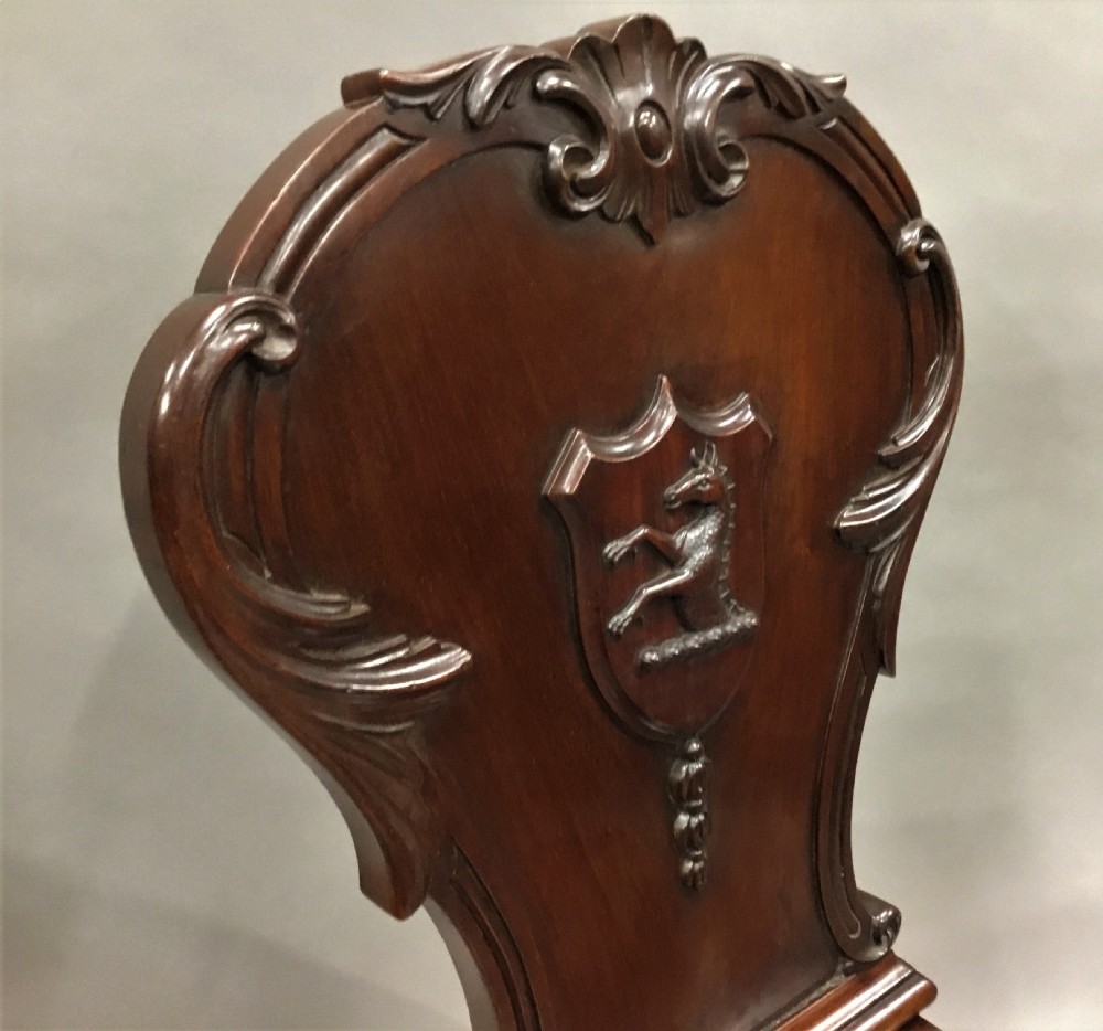 A pair of dark George IV mahogany hall chairs featuring carved backrest scrolls, crests depicting a hippocampus, and turned front legs. View XVII
