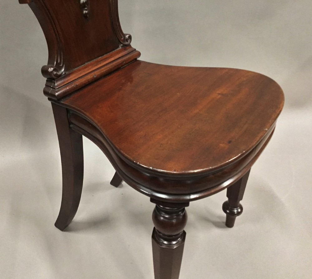 A pair of dark George IV mahogany hall chairs featuring carved backrest scrolls, crests depicting a hippocampus, and turned front legs. View XVIII