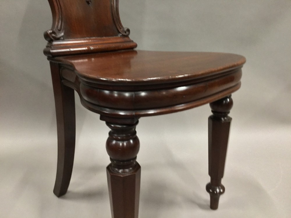 A pair of dark George IV mahogany hall chairs featuring carved backrest scrolls, crests depicting a hippocampus, and turned front legs. View XX
