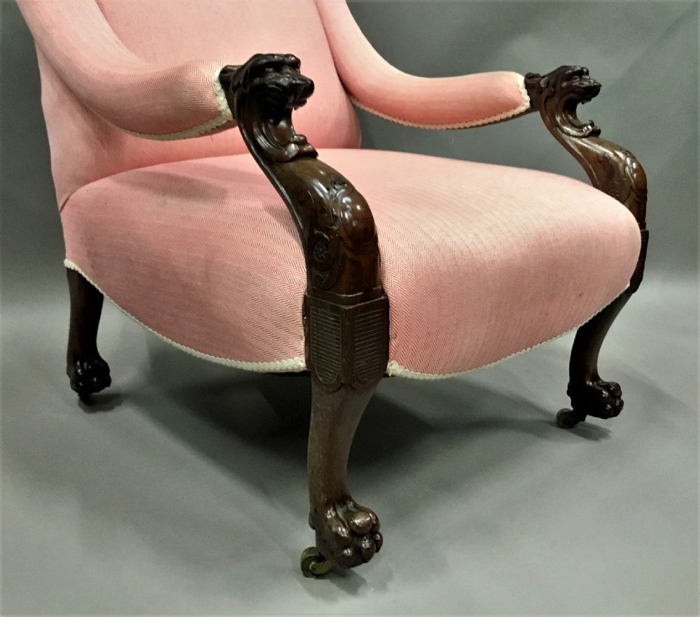 A Regency mahogany armchair upholstered in pink fabric, featuring carved lion-head arm terminals and hairy paw feet on brass castors. View VI
