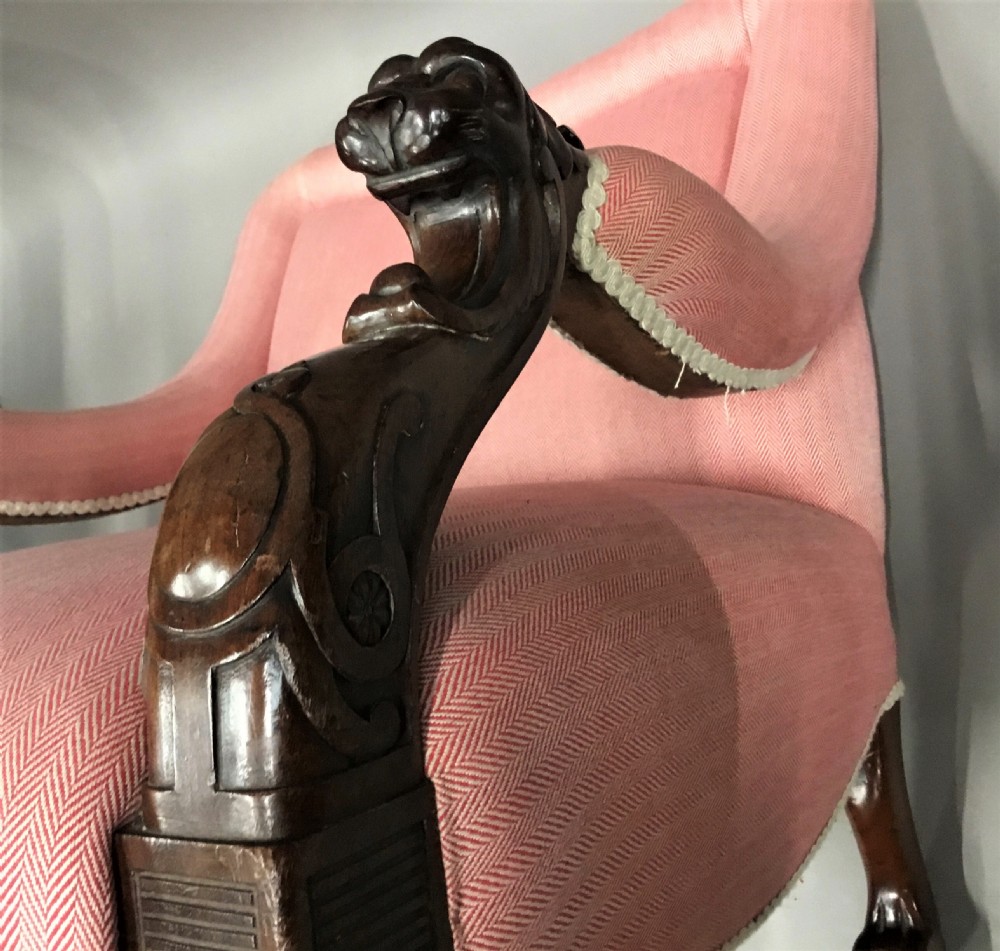 A Regency mahogany armchair upholstered in pink fabric, featuring carved lion-head arm terminals and hairy paw feet on brass castors. View XI