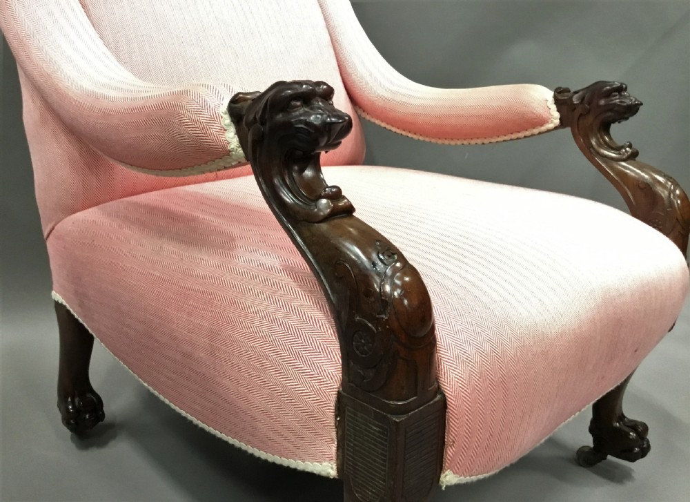A Regency mahogany armchair upholstered in pink fabric, featuring carved lion-head arm terminals and hairy paw feet on brass castors. View XX