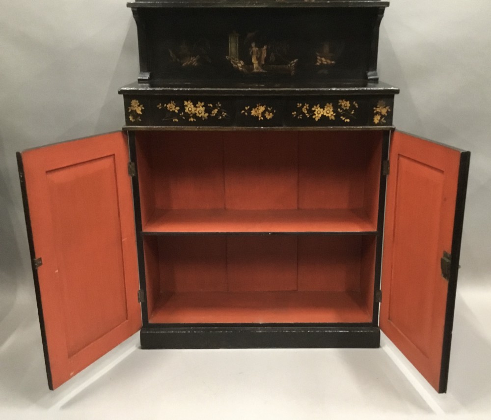 A black lacquered Regency chiffonier side cabinet featuring gold gilded Chinoiserie landscapes, floral borders, a top gallery shelf, and two cupboard doors. View XIV
