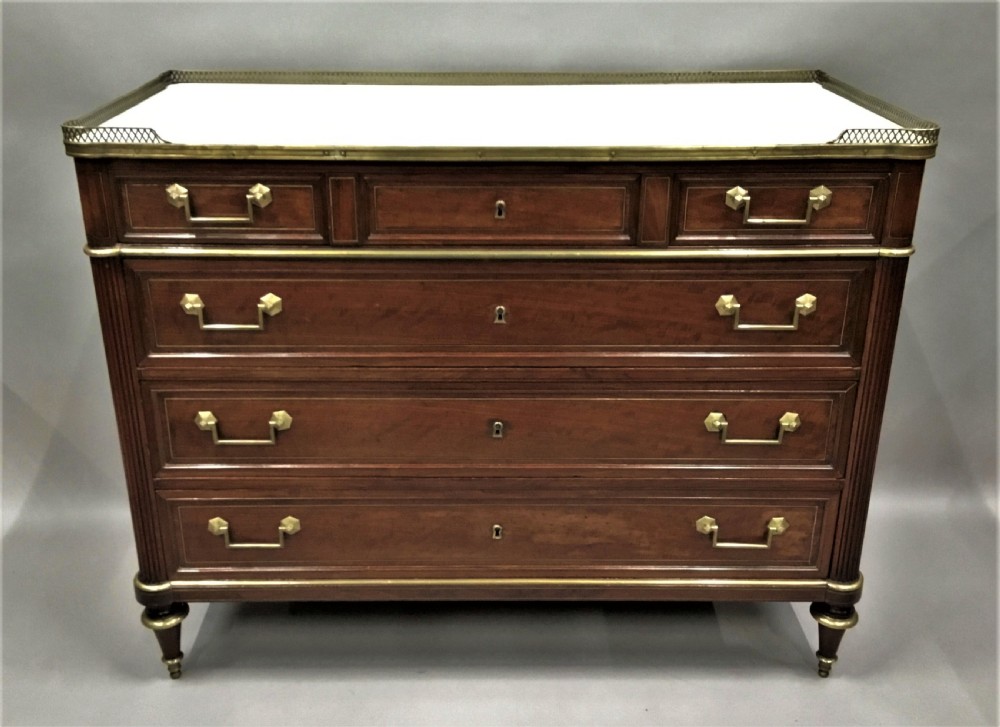 A late 18th-century French Louis XVI neoclassical commode in figured mahogany with a top brass gallery, four drawers, fluted corner stiles, angular brass handles, and turned tapered legs. View V