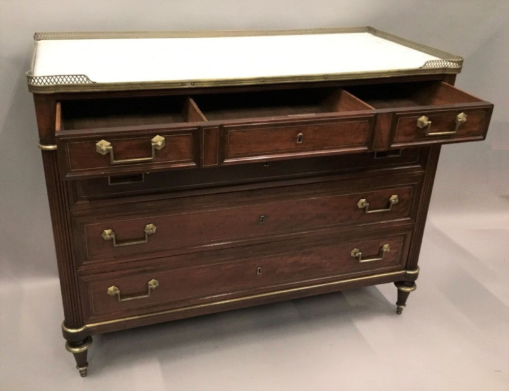 A late 18th-century French Louis XVI neoclassical commode in figured mahogany with a top brass gallery, four drawers, fluted corner stiles, angular brass handles, and turned tapered legs. View VI
