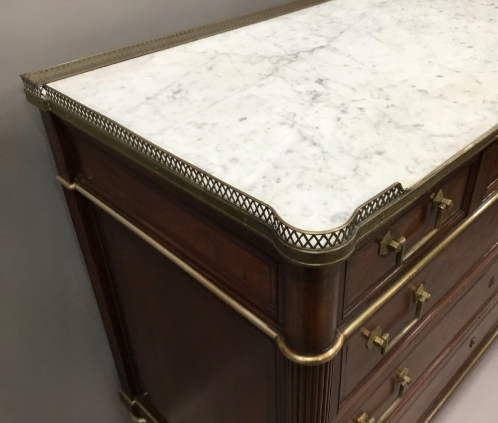 A late 18th-century French Louis XVI neoclassical commode in figured mahogany with a top brass gallery, four drawers, fluted corner stiles, angular brass handles, and turned tapered legs. View IX