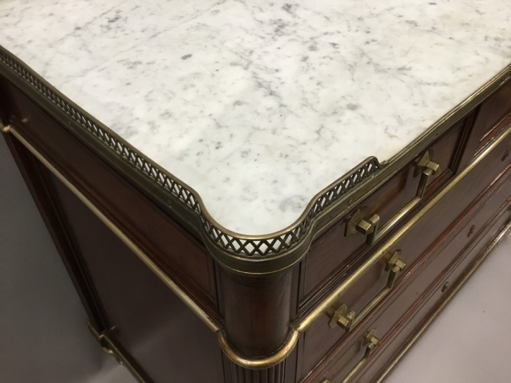 A late 18th-century French Louis XVI neoclassical commode in figured mahogany with a top brass gallery, four drawers, fluted corner stiles, angular brass handles, and turned tapered legs. View X