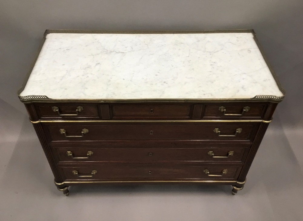 A late 18th-century French Louis XVI neoclassical commode in figured mahogany with a top brass gallery, four drawers, fluted corner stiles, angular brass handles, and turned tapered legs. View XI