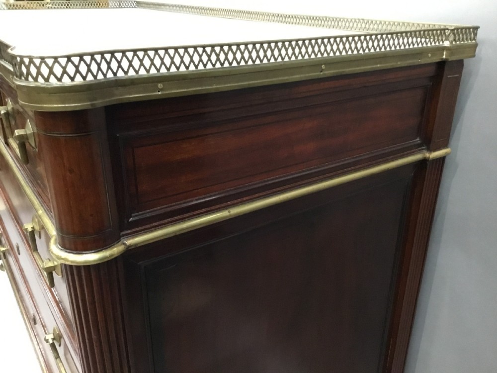 A late 18th-century French Louis XVI neoclassical commode in figured mahogany with a top brass gallery, four drawers, fluted corner stiles, angular brass handles, and turned tapered legs. View XIII