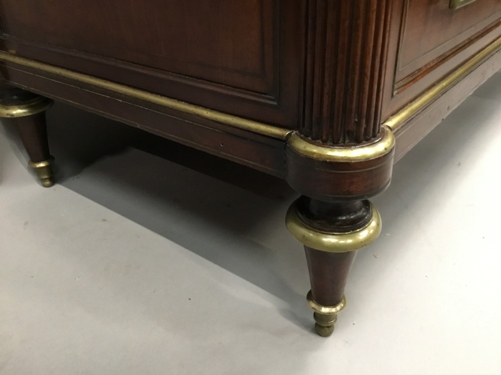 A late 18th-century French Louis XVI neoclassical commode in figured mahogany with a top brass gallery, four drawers, fluted corner stiles, angular brass handles, and turned tapered legs. View XV