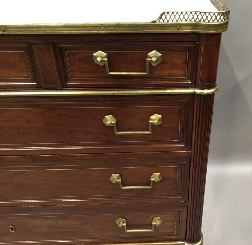A late 18th-century French Louis XVI neoclassical commode in figured mahogany with a top brass gallery, four drawers, fluted corner stiles, angular brass handles, and turned tapered legs. View XVI