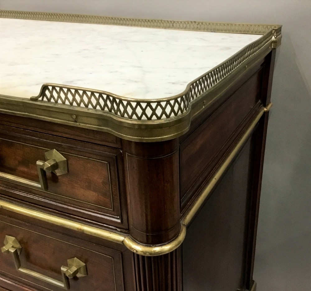 A late 18th-century French Louis XVI neoclassical commode in figured mahogany with a top brass gallery, four drawers, fluted corner stiles, angular brass handles, and turned tapered legs. View XVII