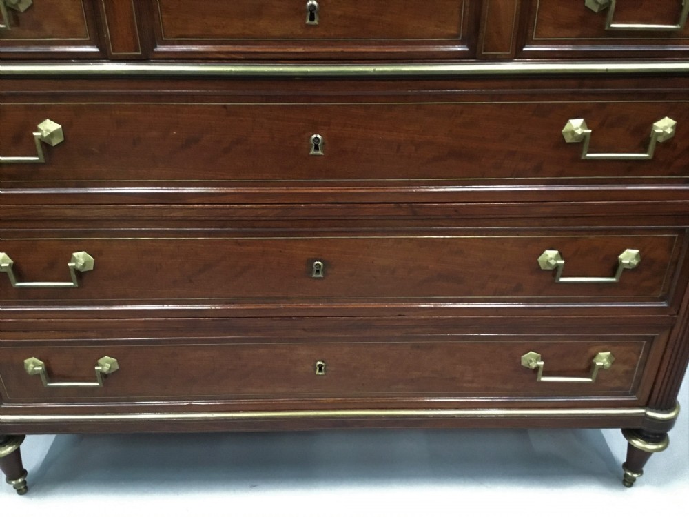 A late 18th-century French Louis XVI neoclassical commode in figured mahogany with a top brass gallery, four drawers, fluted corner stiles, angular brass handles, and turned tapered legs. View XX