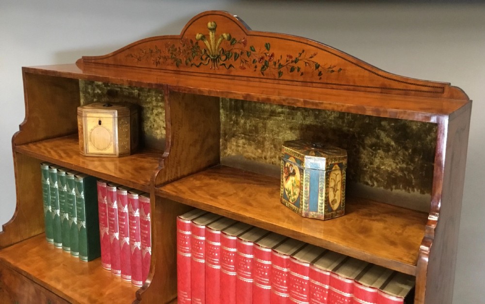 A George III satinwood bookcase cabinet featuring open shelves, painted floral garlands, four drawers with brass drop handles, and square tapered legs. View XIII