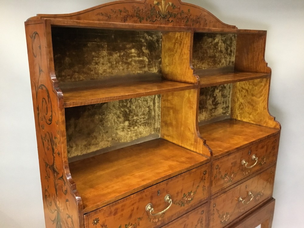 A George III satinwood bookcase cabinet featuring open shelves, painted floral garlands, four drawers with brass drop handles, and square tapered legs. View XVI