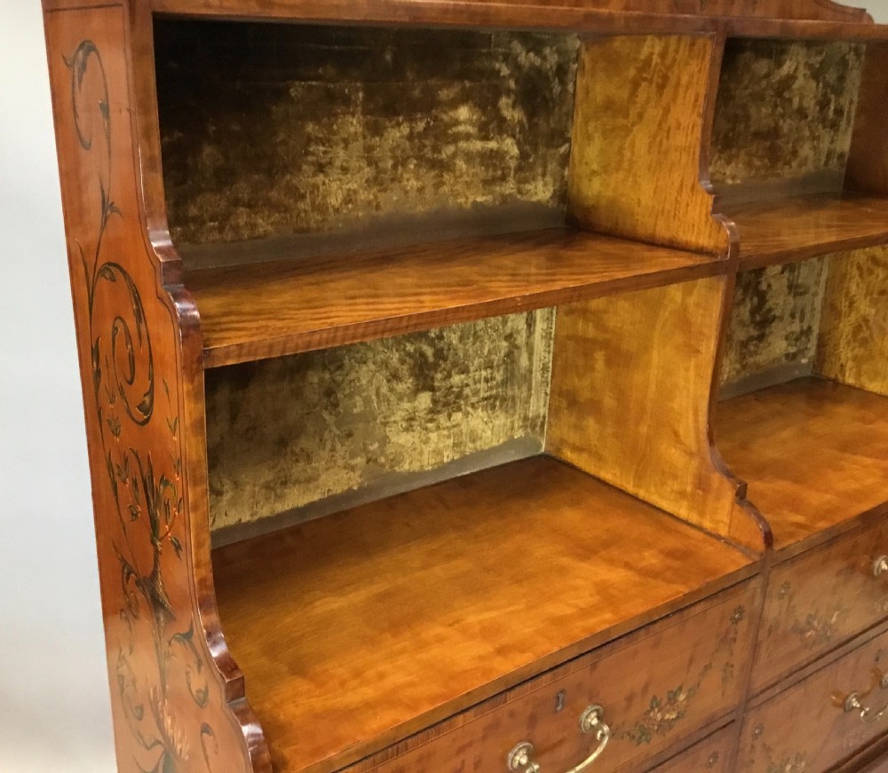 A George III satinwood bookcase cabinet featuring open shelves, painted floral garlands, four drawers with brass drop handles, and square tapered legs. View XVII