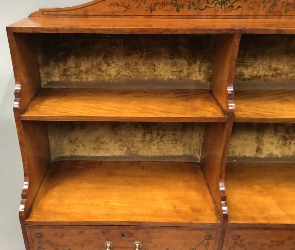 A George III satinwood bookcase cabinet featuring open shelves, painted floral garlands, four drawers with brass drop handles, and square tapered legs. View XVIII