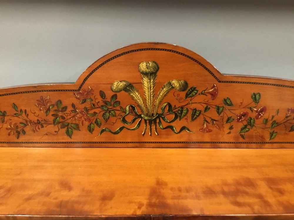 A George III satinwood bookcase cabinet featuring open shelves, painted floral garlands, four drawers with brass drop handles, and square tapered legs. View XIX