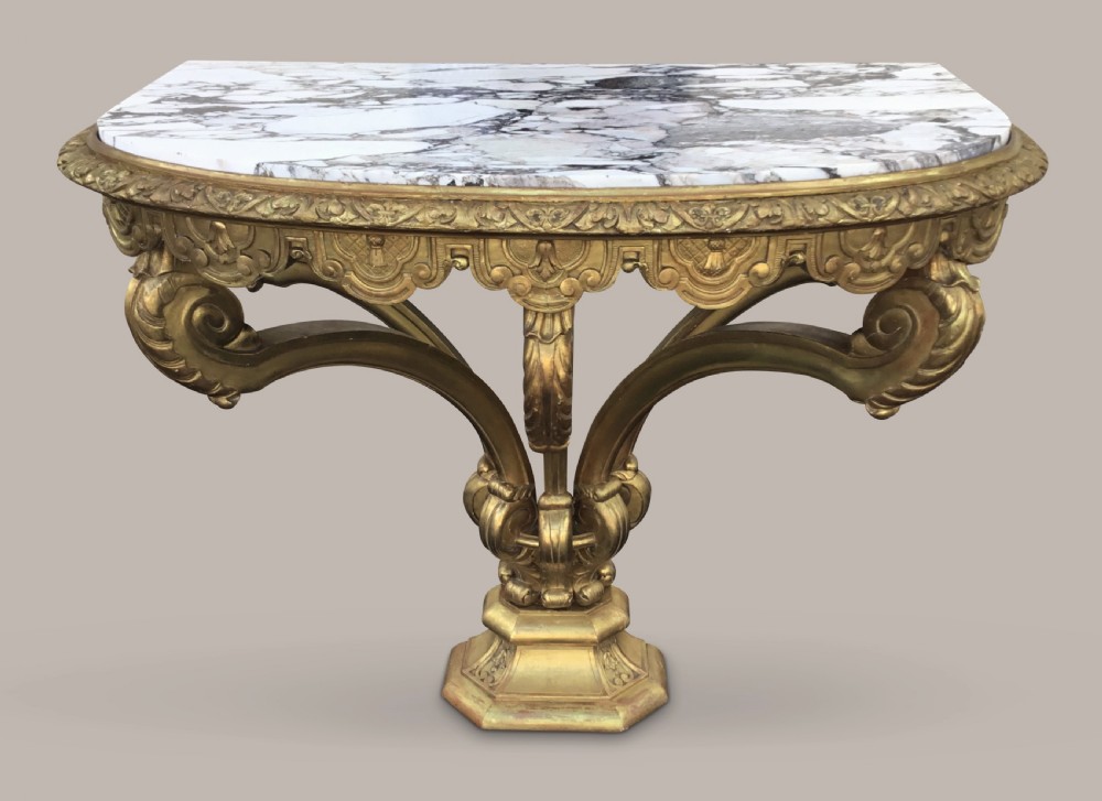 A 19th-century giltwood console table in the Kentian manner featuring a variegated white and grey marble top, carved apron, and central pedestal support with scrolled legs.