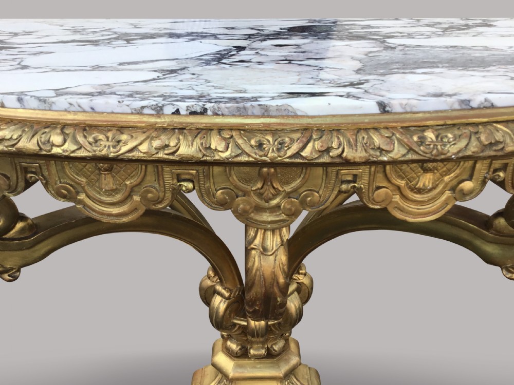 A 19th-century giltwood console table in the Kentian manner featuring a variegated white and grey marble top, carved apron, and central pedestal support with scrolled legs. View VI