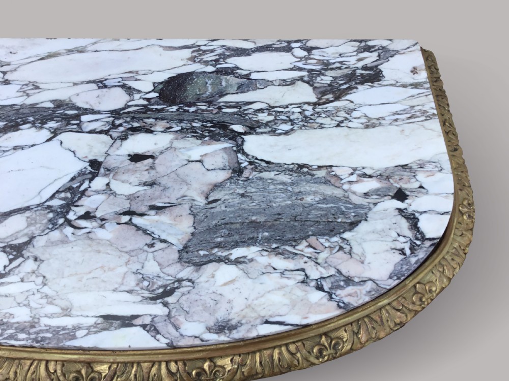 A 19th-century giltwood console table in the Kentian manner featuring a variegated white and grey marble top, carved apron, and central pedestal support with scrolled legs. View X