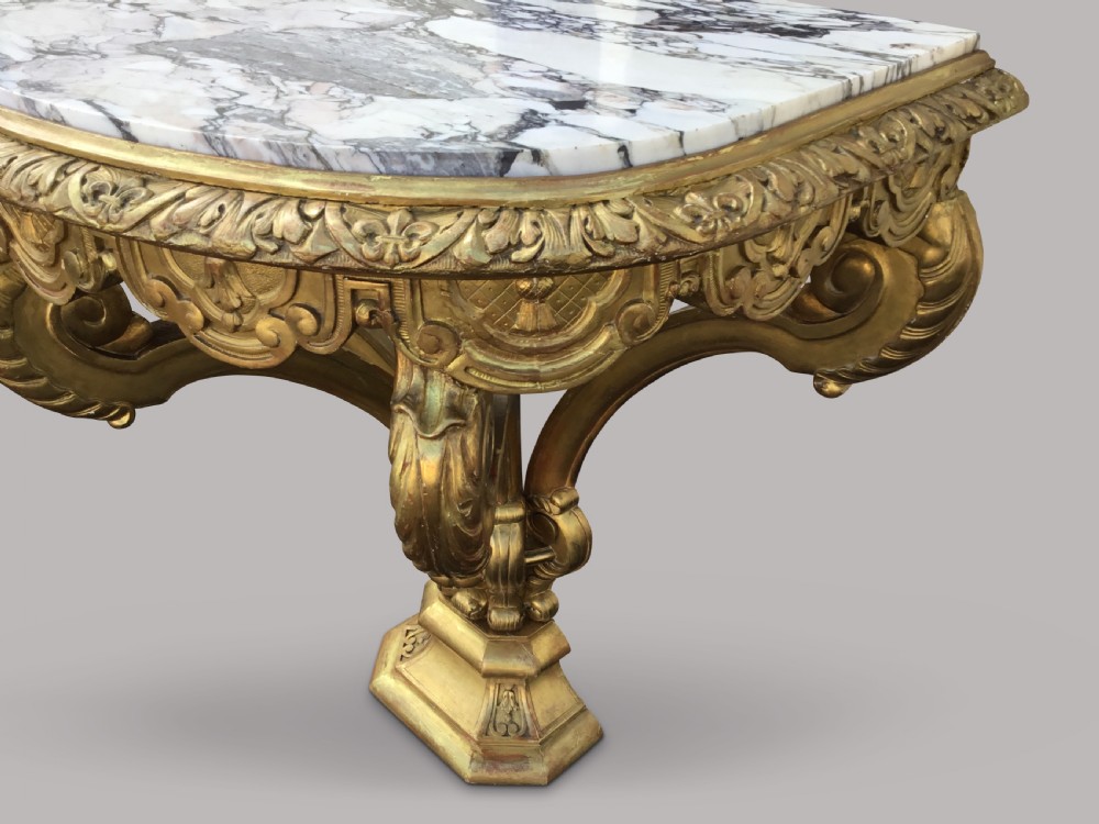 A 19th-century giltwood console table in the Kentian manner featuring a variegated white and grey marble top, carved apron, and central pedestal support with scrolled legs. View XII