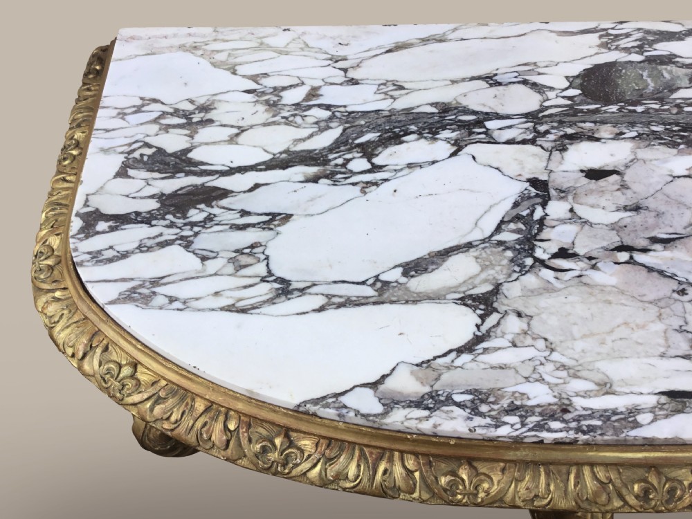 A 19th-century giltwood console table in the Kentian manner featuring a variegated white and grey marble top, carved apron, and central pedestal support with scrolled legs. View XIII
