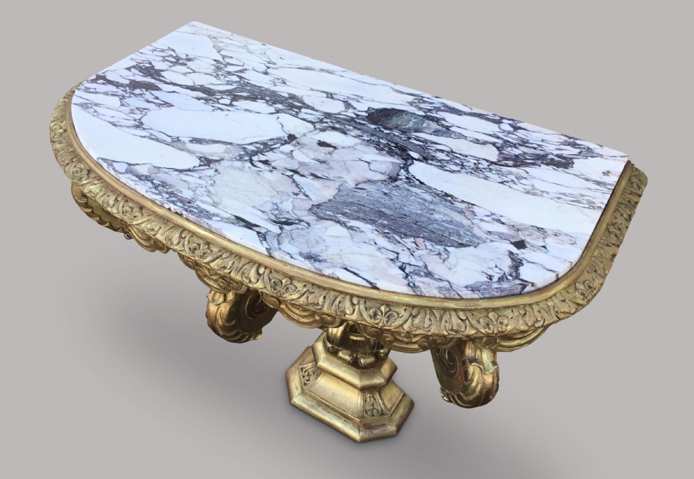 A 19th-century giltwood console table in the Kentian manner featuring a variegated white and grey marble top, carved apron, and central pedestal support with scrolled legs. View XVI