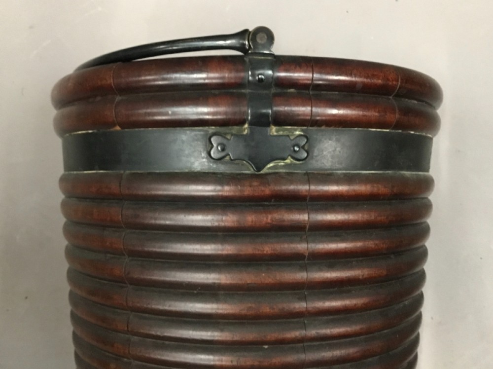 An eighteenth-century mahogany Irish peat bucket featuring a ribbed coopered body, brass banding, and an overhead carrying handle. View VI