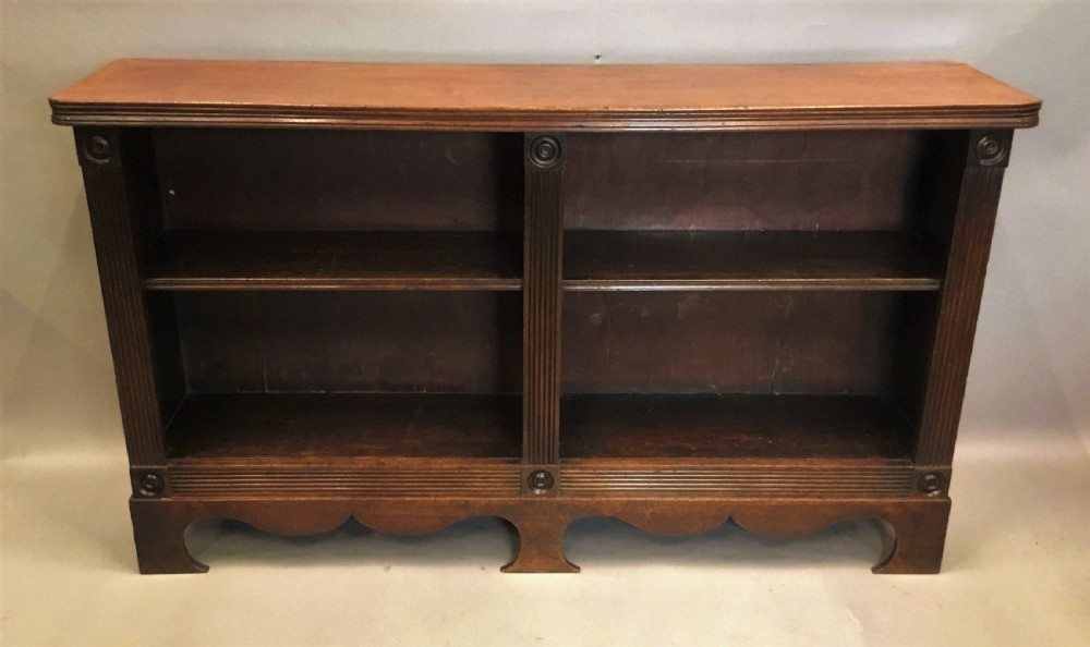 A low Regency mahogany open bookcase featuring two sections with fixed shelving, flanked by fluted pilasters with roundels, set over a shaped apron. View III