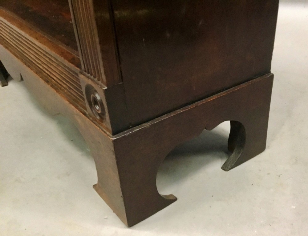 A low Regency mahogany open bookcase featuring two sections with fixed shelving, flanked by fluted pilasters with roundels, set over a shaped apron. View XVI