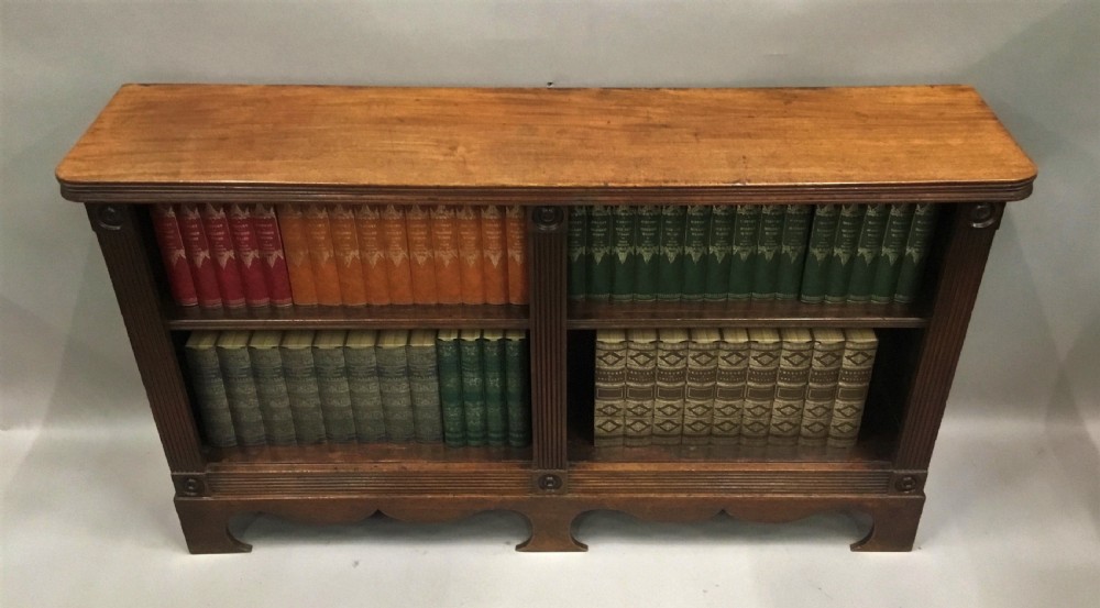 A low Regency mahogany open bookcase featuring two sections with fixed shelving, flanked by fluted pilasters with roundels, set over a shaped apron. View XVII