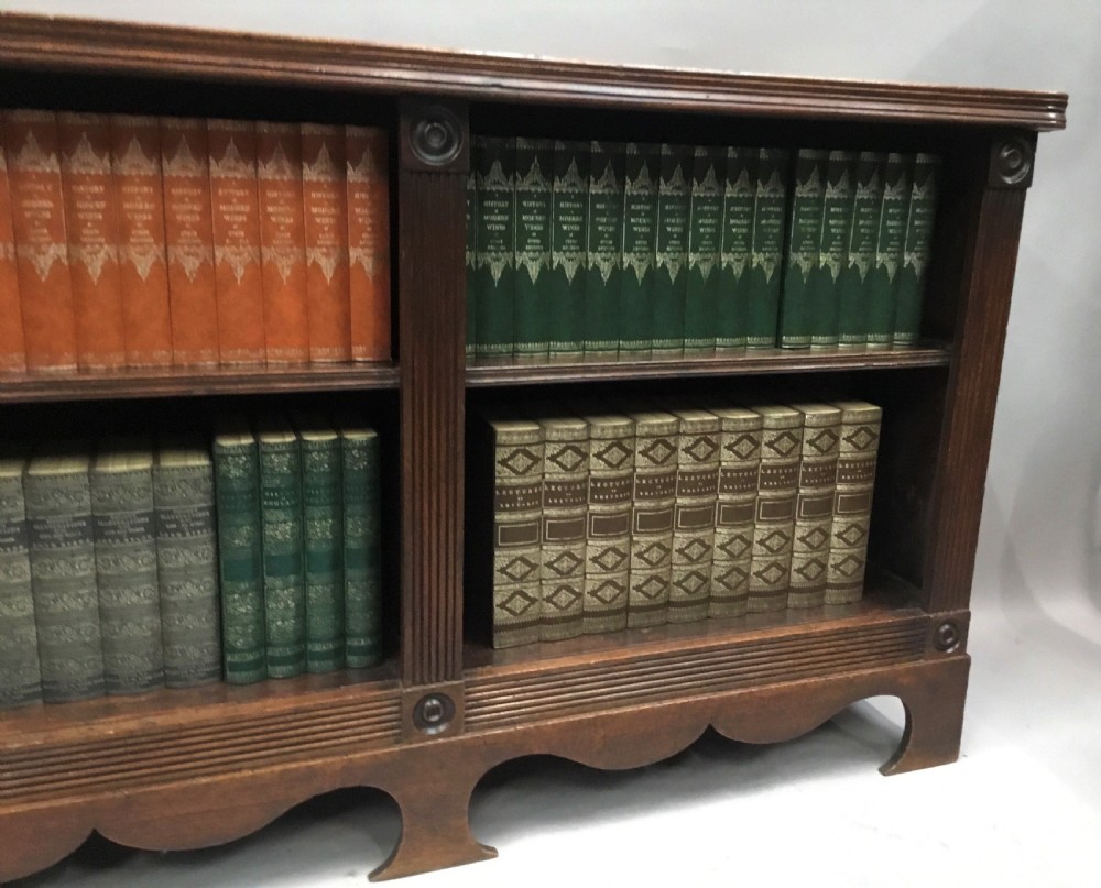 A low Regency mahogany open bookcase featuring two sections with fixed shelving, flanked by fluted pilasters with roundels, set over a shaped apron. View XVIII