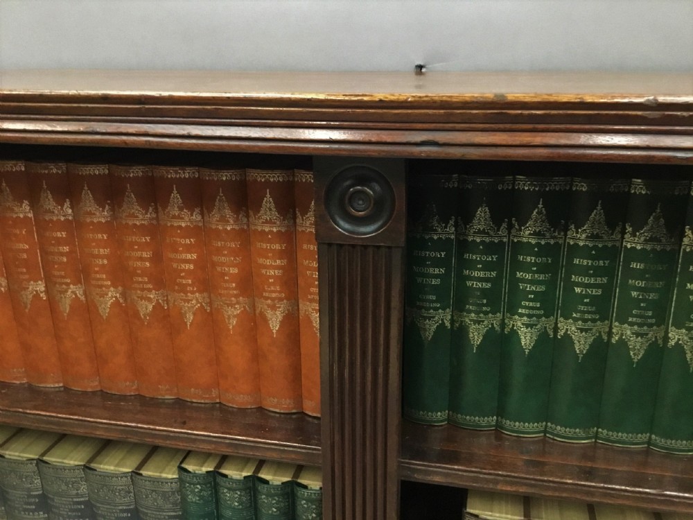 A low Regency mahogany open bookcase featuring two sections with fixed shelving, flanked by fluted pilasters with roundels, set over a shaped apron. View XXI