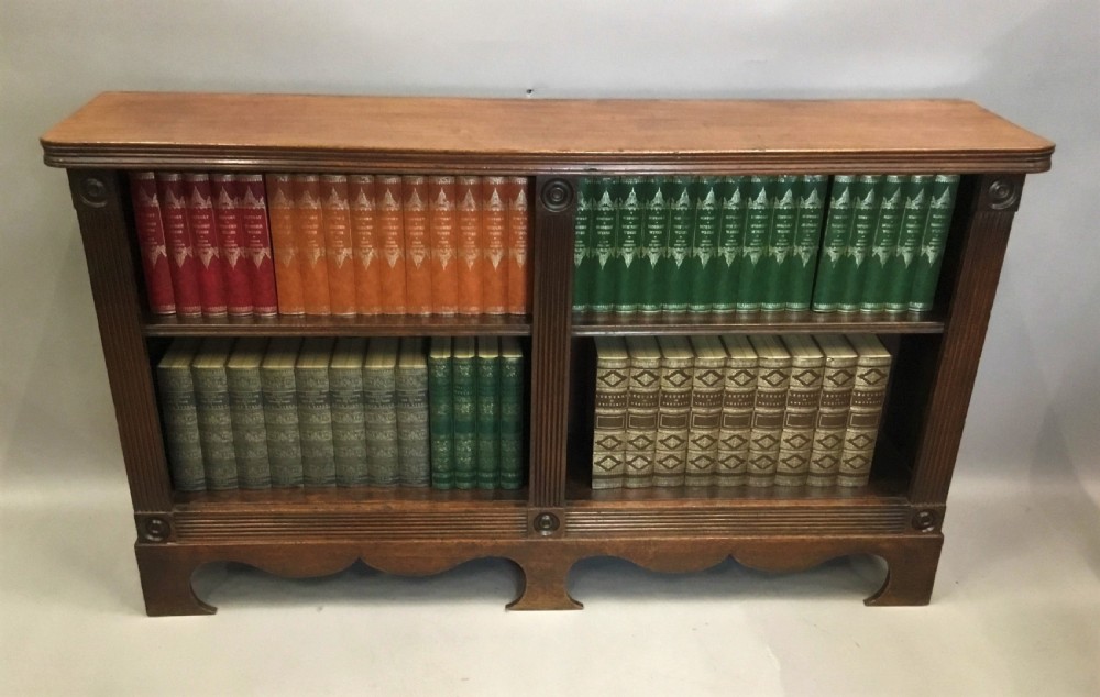 A low Regency mahogany open bookcase featuring two sections with fixed shelving, flanked by fluted pilasters with roundels, set over a shaped apron. View XXIV