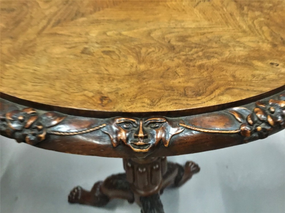 A circular George IV pollard oak occasional table featuring a segmented veneer top, carved rim with floral details, and a tripod pedestal base with carved feet. View VI