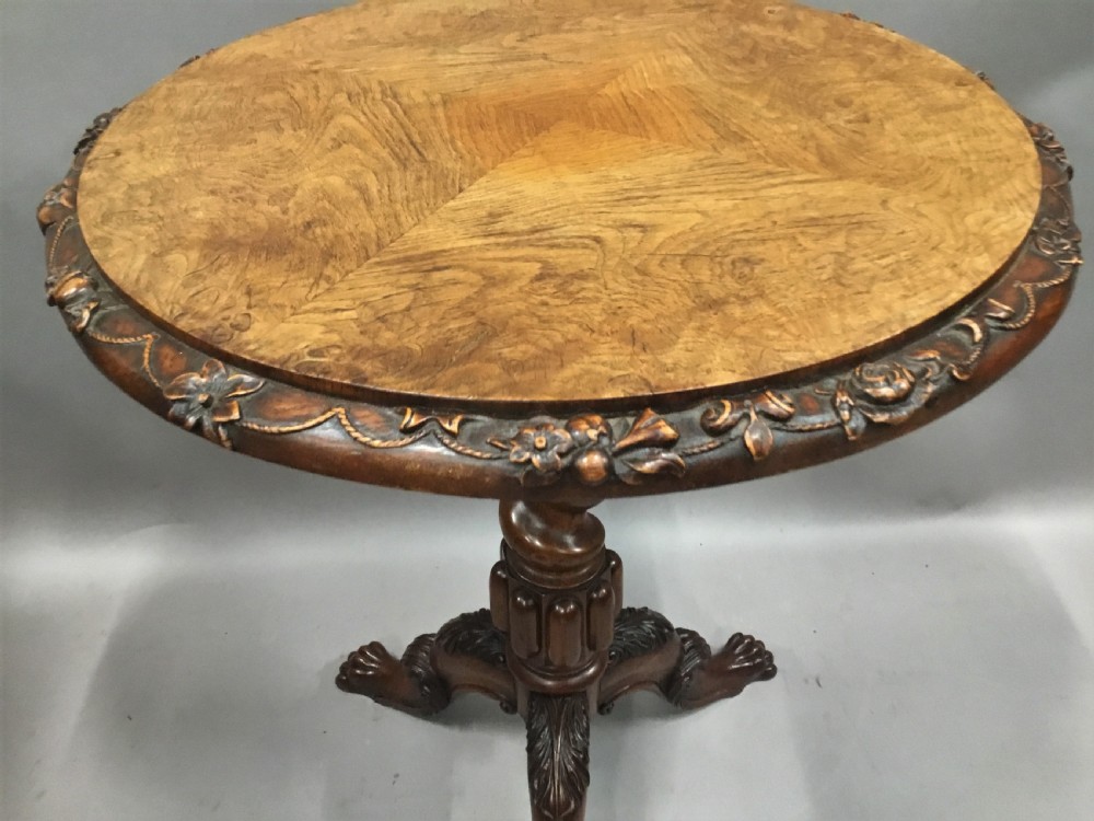 A circular George IV pollard oak occasional table featuring a segmented veneer top, carved rim with floral details, and a tripod pedestal base with carved feet. View VII