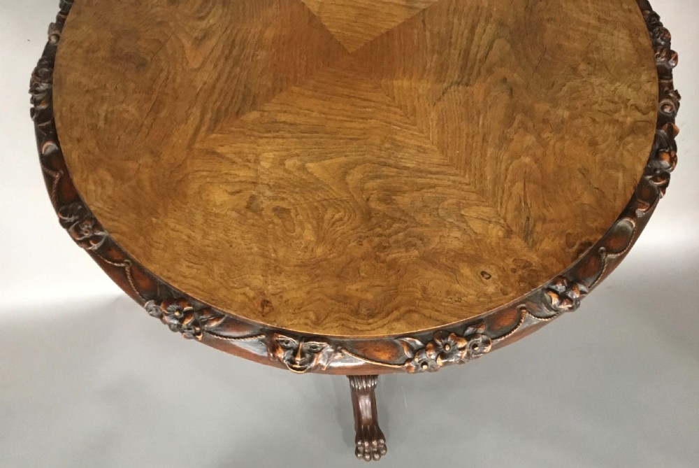 A circular George IV pollard oak occasional table featuring a segmented veneer top, carved rim with floral details, and a tripod pedestal base with carved feet. View IX