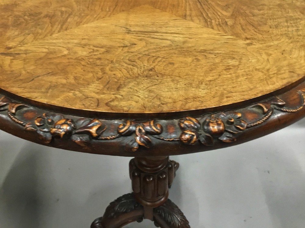 A circular George IV pollard oak occasional table featuring a segmented veneer top, carved rim with floral details, and a tripod pedestal base with carved feet. View X