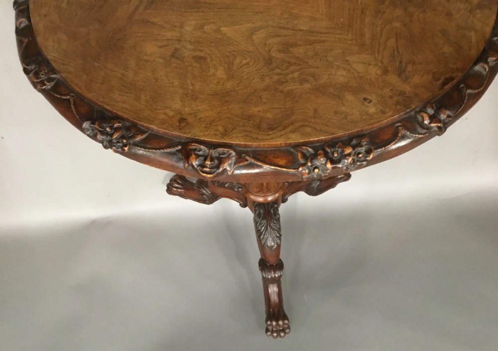 A circular George IV pollard oak occasional table featuring a segmented veneer top, carved rim with floral details, and a tripod pedestal base with carved feet. View XII
