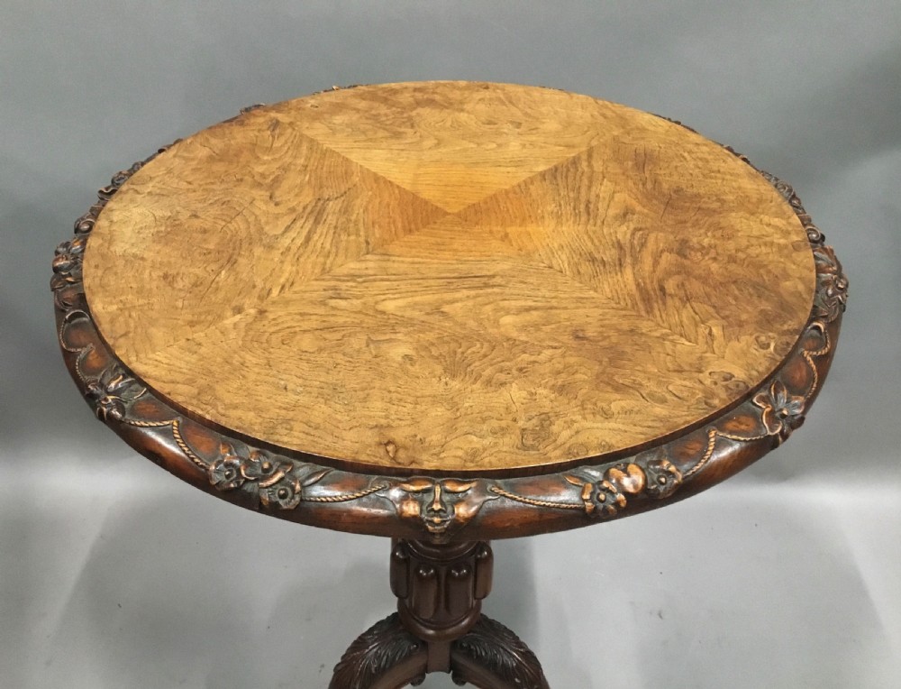 A circular George IV pollard oak occasional table featuring a segmented veneer top, carved rim with floral details, and a tripod pedestal base with carved feet. View XIII