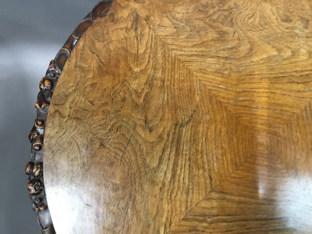 A circular George IV pollard oak occasional table featuring a segmented veneer top, carved rim with floral details, and a tripod pedestal base with carved feet. View XIV