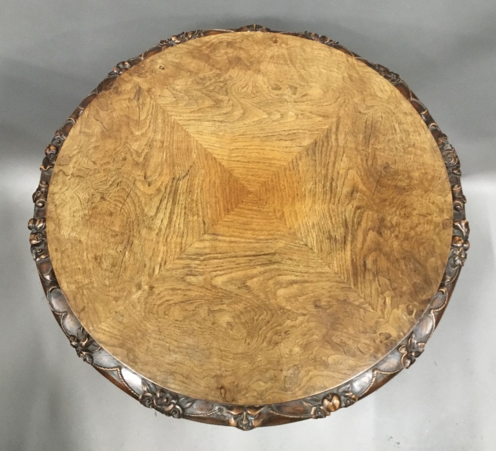 A circular George IV pollard oak occasional table featuring a segmented veneer top, carved rim with floral details, and a tripod pedestal base with carved feet. View XVIII