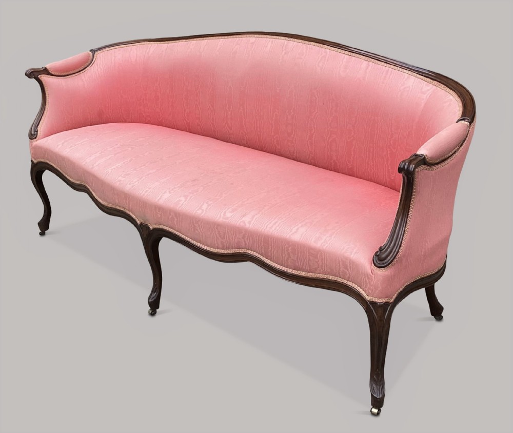 A George III Hepplewhite mahogany settee featuring pink damask upholstery, serpentine backline, and carved cabriole legs on brass castors.