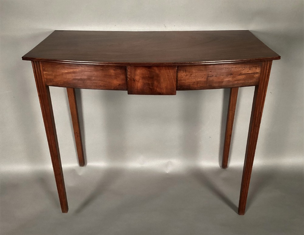 A George III mahogany bow-fronted side table featuring a curved top, frieze panel, and four square tapered legs.