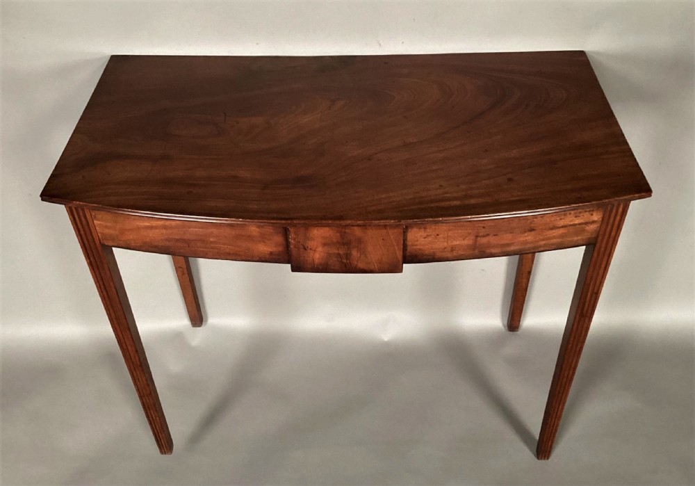 A George III mahogany bow-fronted side table featuring a curved top, frieze panel, and four square tapered legs. View II