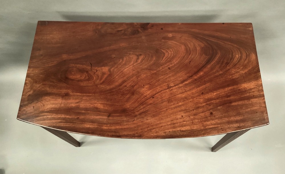 A George III mahogany bow-fronted side table featuring a curved top, frieze panel, and four square tapered legs. View III
