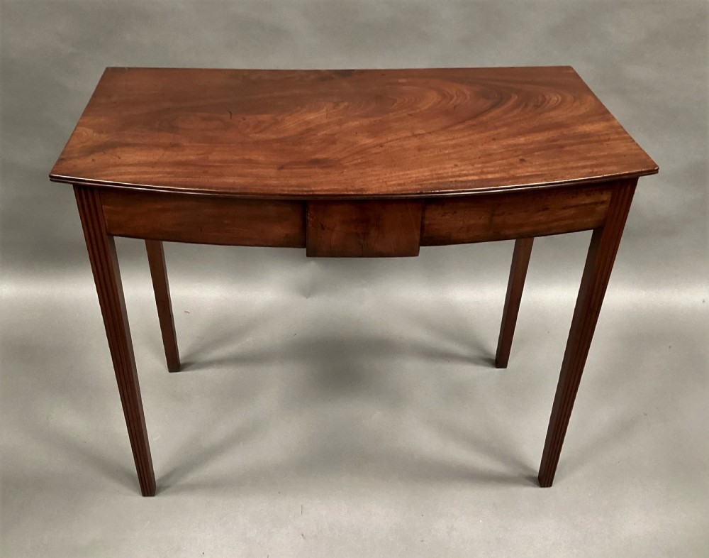 A George III mahogany bow-fronted side table featuring a curved top, frieze panel, and four square tapered legs. View VI
